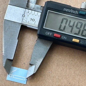 May include: A digital caliper measuring a small, light blue rectangular object. The caliper reads 0.498 inches.