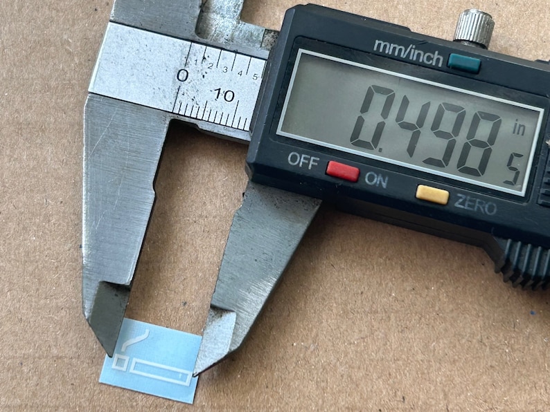 May include: A digital caliper measuring a small, light blue rectangular object. The caliper reads 0.498 inches.