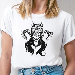 Peut inclure: T-shirt blanc avec un motif noir et blanc d'une femme avec une t&ecirc;te de loup et deux haches.
