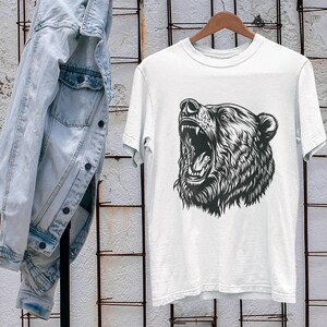 以下が含まれることがあります： 咆哮する熊の頭部の白黒イラストが描かれた白いTシャツ