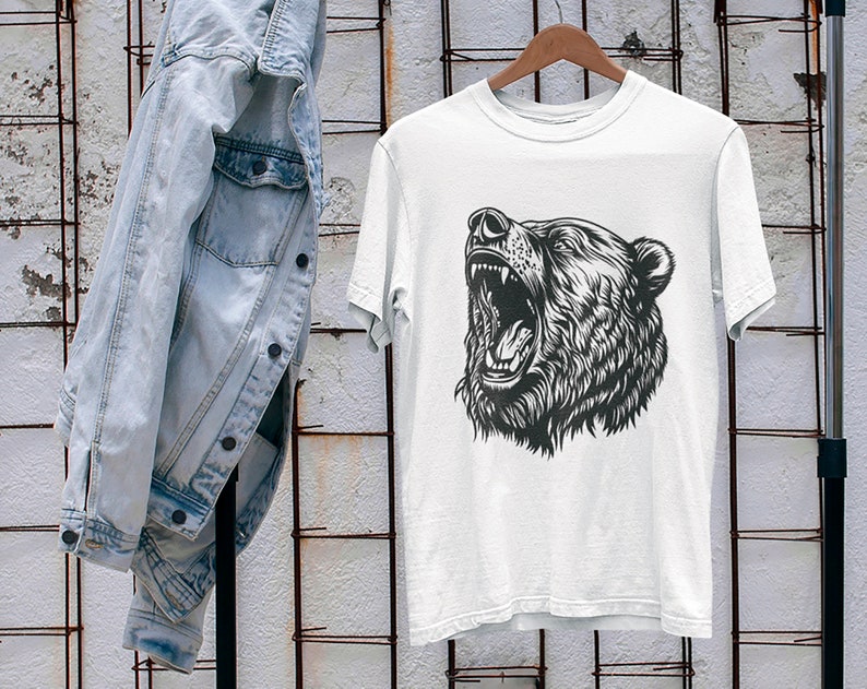 以下が含まれることがあります： 咆哮する熊の頭部の白黒イラストが描かれた白いTシャツ