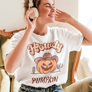 Peut inclure: T-shirt blanc avec un graphique de citrouille portant un chapeau de cowboy et le texte "Howdy Pumpkin".