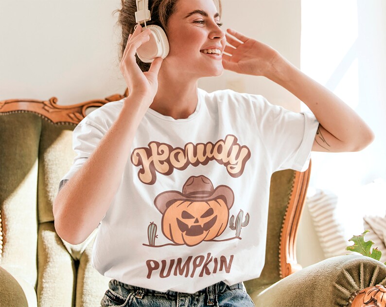 Peut inclure: T-shirt blanc avec un graphique de citrouille portant un chapeau de cowboy et le texte "Howdy Pumpkin".