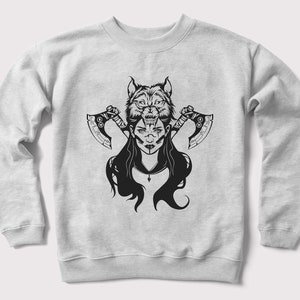 Peut inclure: Un sweat-shirt gris avec un imprim&eacute; graphique noir et blanc d'une femme avec une t&ecirc;te de loup et deux haches.