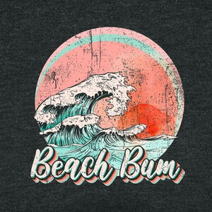 May include: Dark gray t-shirt with a distressed graphic of a wave, a setting sun, and a pink and blue circle. The text "Beach Bum" is in a retro font.