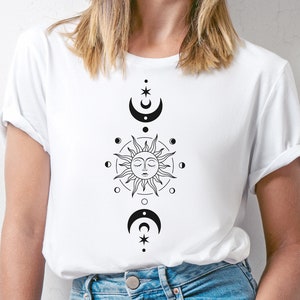 K&ouml;nnte beinhalten: Wei&szlig;es T-Shirt mit einem schwarzen Sonnen- und Monddesign. Die Sonne hat ein Gesicht und ist von einem Kreis aus kleineren Monden umgeben. Der Mond ist halbmondf&ouml;rmig und hat einen Stern dar&uuml;ber.
