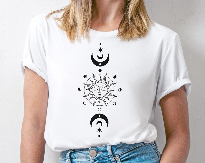 K&ouml;nnte beinhalten: Wei&szlig;es T-Shirt mit einem schwarzen Sonnen- und Monddesign. Die Sonne hat ein Gesicht und ist von einem Kreis aus kleineren Monden umgeben. Der Mond ist halbmondf&ouml;rmig und hat einen Stern dar&uuml;ber.