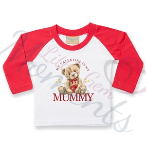 Könnte beinhalten: Weißes Langarmshirt mit roten Ärmeln. Das Shirt hat ein Motiv mit einem Teddybär, der eine herzförmige Schachtel hält, und den Text "My Valentine is my Mummy".