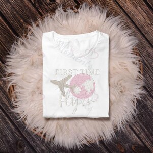 May include: White t-shirt with the text "First Time Flyers" and an embroidered airplane and globe. The globe is pink and the airplane is beige.