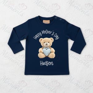 May include: Navy blue long-sleeved top with the text "Happy Mother's Day" and the name "Hudson". It features a teddy bear holding a blue heart. The top has two buttons on the shoulder.
