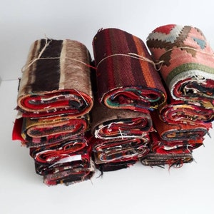 May include: A stack of rolled up colorful fabric scraps, some with a striped pattern, others with a more intricate design. The fabric is a mix of red, brown, and beige.