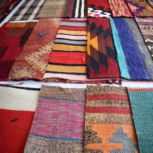 Puede incluir: Una colección de alfombras rectangulares tejidas de colores con varios patrones y diseños. Las alfombras presentan una mezcla de colores, incluyendo rojo, azul, naranja y marrón, con patrones geométricos y a rayas. Los textiles se exhiben sobre una superficie blanca.