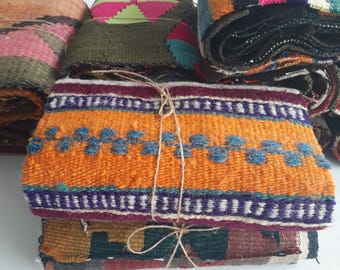 Può includere: Una pila di pezzi di tessuto colorato, legati con spago. I tessuti presentano vari motivi e colori, tra cui arancione, blu, viola, rosa e verde. I tessuti sembrano essere tessuti a mano, con trame e dettagli visibili.