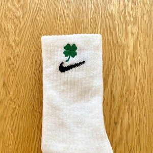 May include: White athletic socks with a black Nike swoosh and a green four-leaf clover embroidered on the top.
