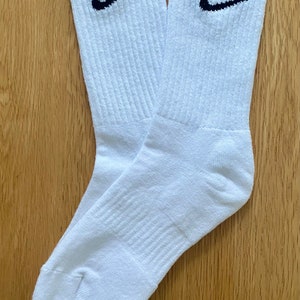 May include: A pair of white athletic socks with black Nike logos. One sock has the letters "VB" above the logo.