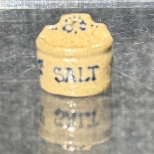 May include: A small, ceramic salt container with a lid. The container is cream-colored with black lettering that reads "SALT".