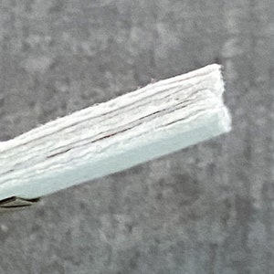 May include: Close-up of a white, layered, fabric material. The fabric is folded and has a slightly textured surface.