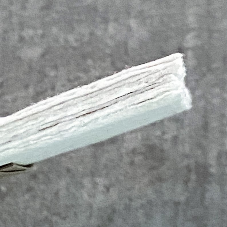 May include: Close-up of a white, layered, fabric material. The fabric is folded and has a slightly textured surface.