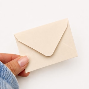 Puede incluir: Un sobre peque&ntilde;o y rectangular de color crema s&oacute;lido. El sobre presenta un dise&ntilde;o cl&aacute;sico de solapa triangular que est&aacute; doblado hacia abajo para cerrar la abertura. El papel tiene una textura suave y mate con un aspecto limpio y sencillo.