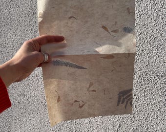 May include: A sheet of handmade paper with embedded dried leaves and ferns. The paper is a light beige color and has a textured surface.