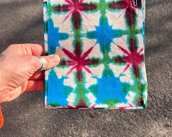 May include: A stack of fabric squares with a tie-dye pattern in shades of blue, green, pink, and white.
