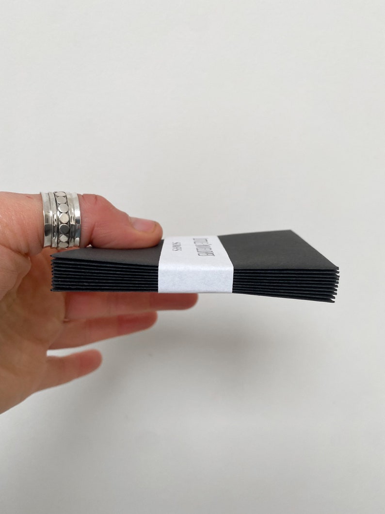 May include: A stack of black notecards held by a hand, with a white band wrapped around the middle. The band features the text "Wild Letter" and "Notes" in a minimalist font. The cards are stacked neatly.