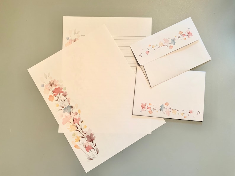 May include: Stationery set featuring white paper and envelopes adorned with a watercolor floral design in pastel colors. The set includes lined and unlined paper, along with matching envelopes, perfect for letters and notes.
