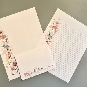 May include: Stationery set featuring a floral design in soft pastel colors. The set includes a lined writing sheet, a blank sheet, and an envelope. The floral design is on the corner of each piece, adding a delicate touch.