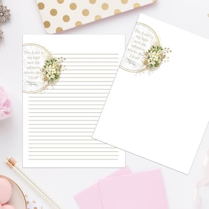 Op de afbeelding: Twee witte, gestreepte vellen papier met een gouden rand en een bloemmotief. De tekst op het papier luidt "De Heer is mijn licht en mijn redding; wie zal ik vrezen?"