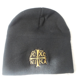May include: Black beanie hat with a gold embroidered emblem featuring a cross and Greek letters. The hat is made of a knitted material and is designed to be worn on the head.