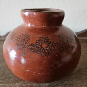 May include: A brown terracotta vase with a floral design in black paint. The vase has a rounded body and a wide mouth.