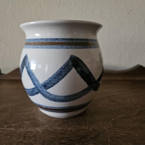 May include: A white ceramic vase with blue and brown geometric patterns. The vase has a rounded body and a wide opening.