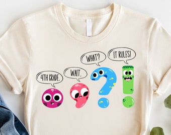 May include: A beige t-shirt with a graphic of cartoon punctuation marks. The text on the shirt reads "4th Grade", "Wait", "What?", and "It Rules!"