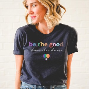 Może przedstawiać: Szary t-shirt w kolorze ciemnego melanżu z napisem "be the good choose kindness" w kolorach tęczy. Pod napisem znajduje się tęczowe serce.