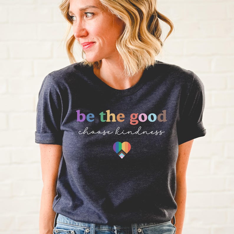 Może przedstawiać: Szary t-shirt w kolorze ciemnego melanżu z napisem "be the good choose kindness" w kolorach tęczy. Pod napisem znajduje się tęczowe serce.