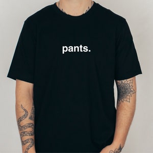 May include: Black t-shirt with the word "pants." printed in white, centered on the chest. The shirt has short sleeves and a crew neck. The fabric appears to be a soft cotton blend.