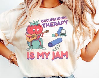 May include: A white t-shirt with a cartoon strawberry playing a guitar. The text "Occupational Therapy is my jam" is printed on the shirt.
