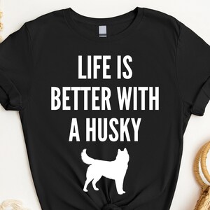 May include: Black t-shirt with white text that reads "Life is better with a husky". A white silhouette of a husky dog is below the text.