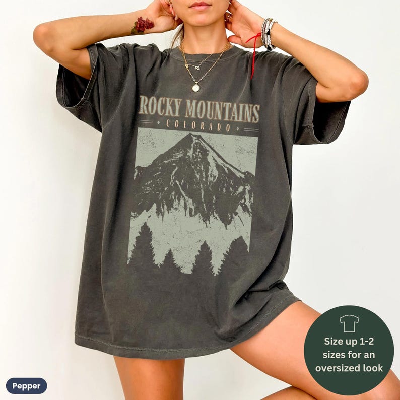 May include: A dark gray oversized t-shirt with a vintage graphic print of the Rocky Mountains in Colorado. The graphic features a mountain range with trees in the foreground. The text "Rocky Mountains - Colorado -" is printed above the graphic.