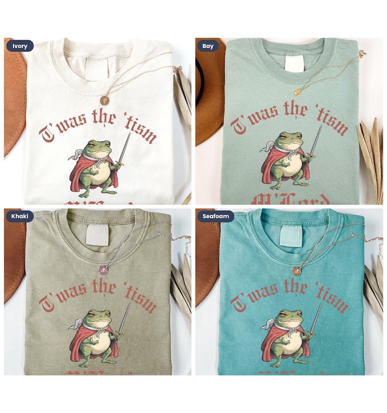 May include: Four different colored t-shirts with a graphic print of a frog wearing a red cape and holding a sword. The text on the shirts reads "T'was the tism". The shirts are available in ivory, khaki, bay, and seafoam.