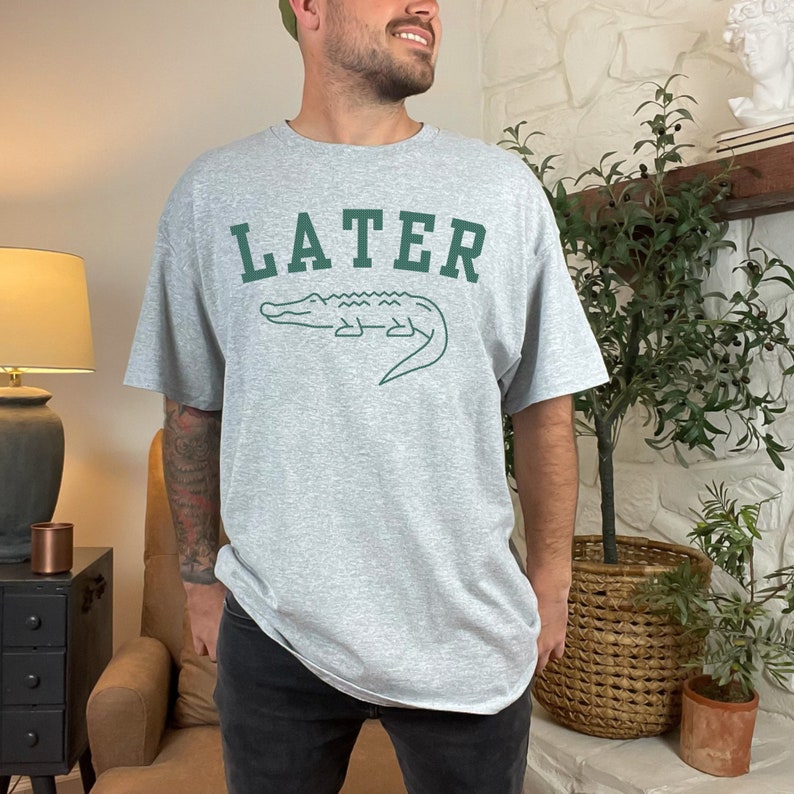 May include: A gray t-shirt with a green alligator graphic and the word "LATER" in green letters.