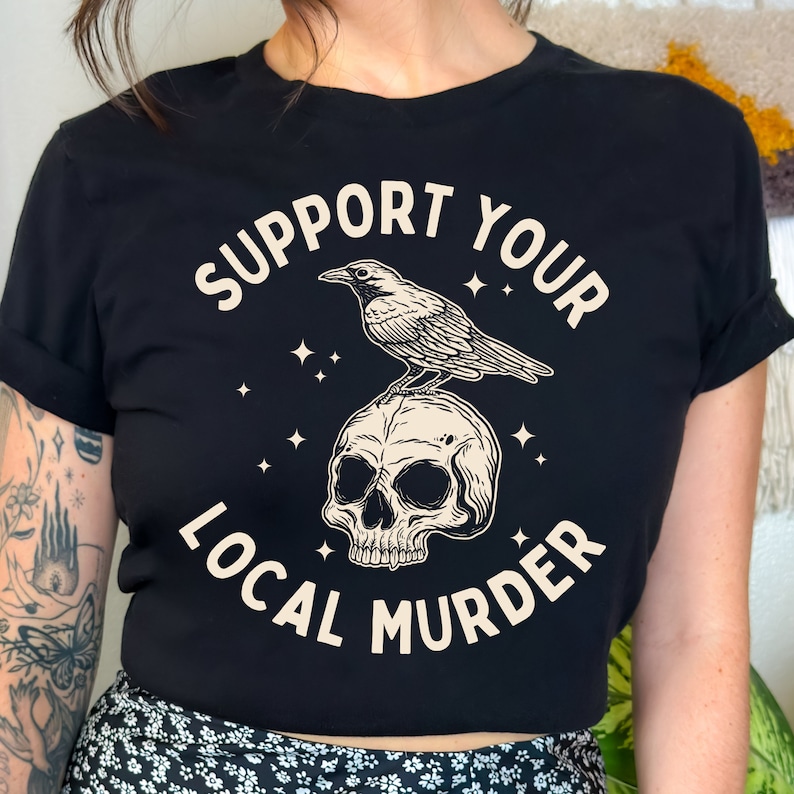 May include: Black cropped t-shirt with a white graphic design. The graphic features a skull with a crow perched on top. The text "Support Your Local Murder" is written around the skull and crow.