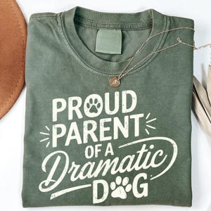 May include: A green t-shirt with the text "Proud Parent of a Dramatic Dog" in white with a paw print graphic.
