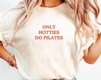 May include: A white t-shirt with the text "ONLY HOTTIES DO PILATES" printed in red.