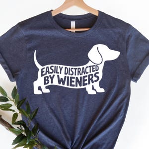 May include: A navy blue t-shirt with a white dachshund silhouette and the text "Easily Distracted By Wieners".