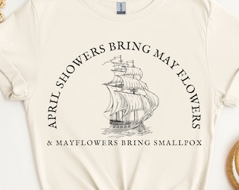 May include: A beige t-shirt with a black graphic print of a ship and the text "April showers bring May flowers & Mayflowers bring smallpox".