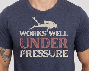 May include: A navy blue t-shirt with a vintage-style graphic of a scuba diver and the text "WORKS WELL UNDER PRESSURE".