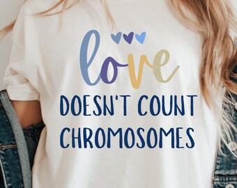 May include: A white t-shirt with the text "love doesn't count chromosomes" in blue and yellow lettering. There are three small blue hearts above the word "love".