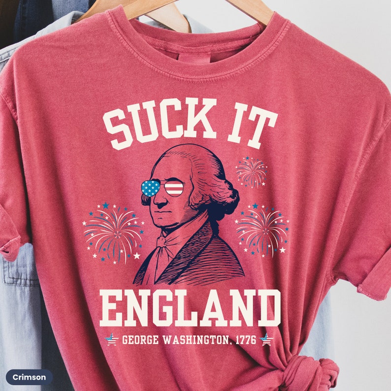 May include: Red t-shirt with a white graphic of George Washington wearing sunglasses and fireworks. The text "SUCK IT ENGLAND" is above the image and "GEORGE WASHINGTON, 1776" is below the image.