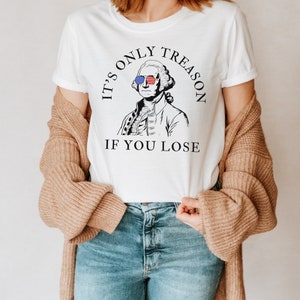 May include: White t-shirt featuring a black and white illustration of George Washington wearing sunglasses with an American flag design. The text on the shirt reads "It's only treason if you lose."